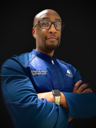 A person wearing glasses and a blue jacket with his arms crossed

Description automatically generated
