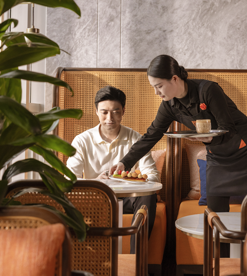 A female Chinese server in a black shirt clears the table for a guest