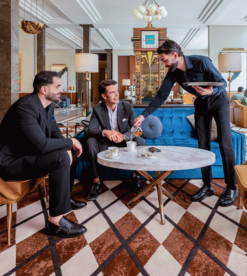 A server hands drinks to two hotel guests as they relax in a hotel lounge