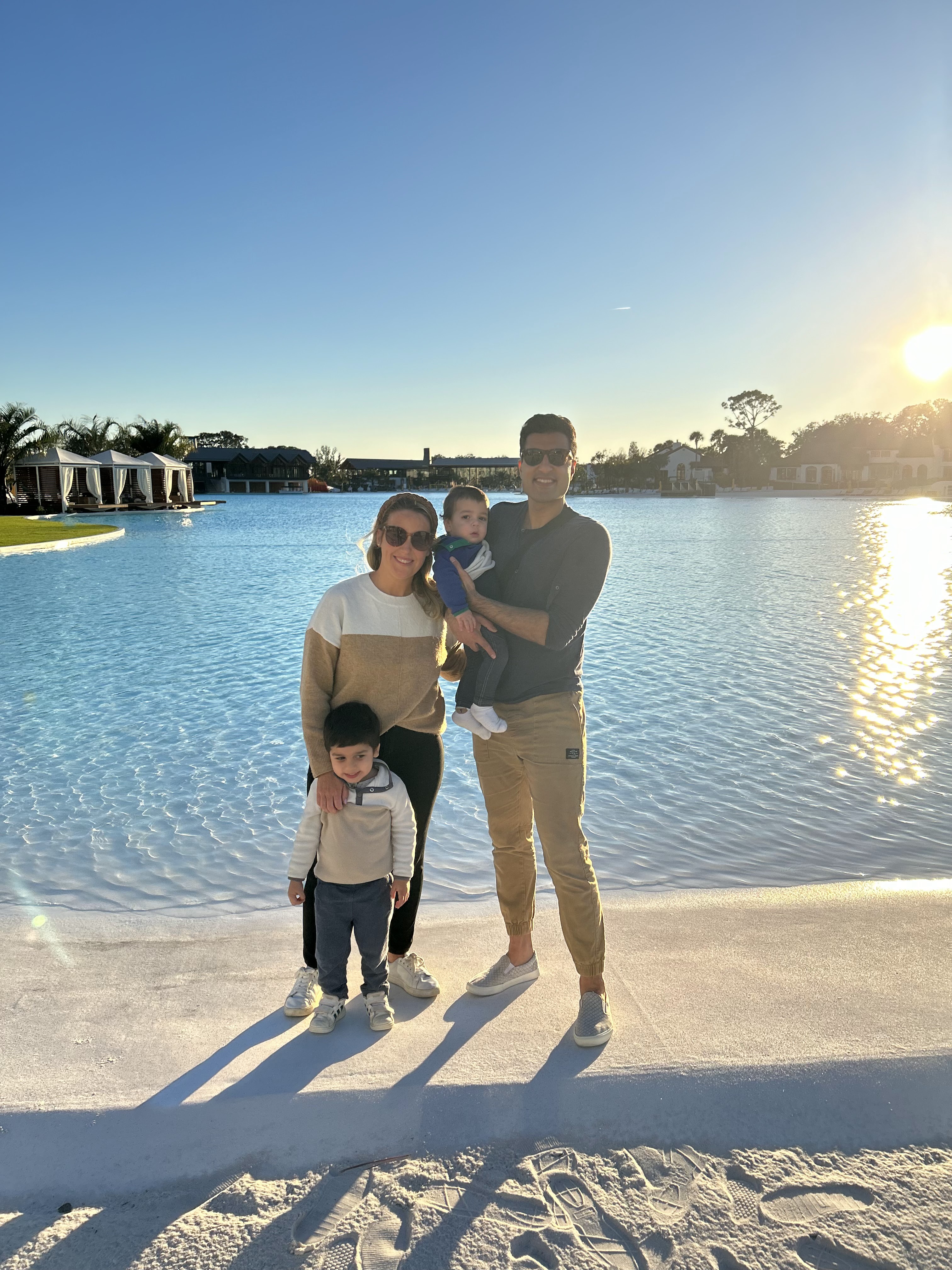 A married couple with a baby and toddler stand in front a wade in pool during sunset at a Hilton resort in Orlando.