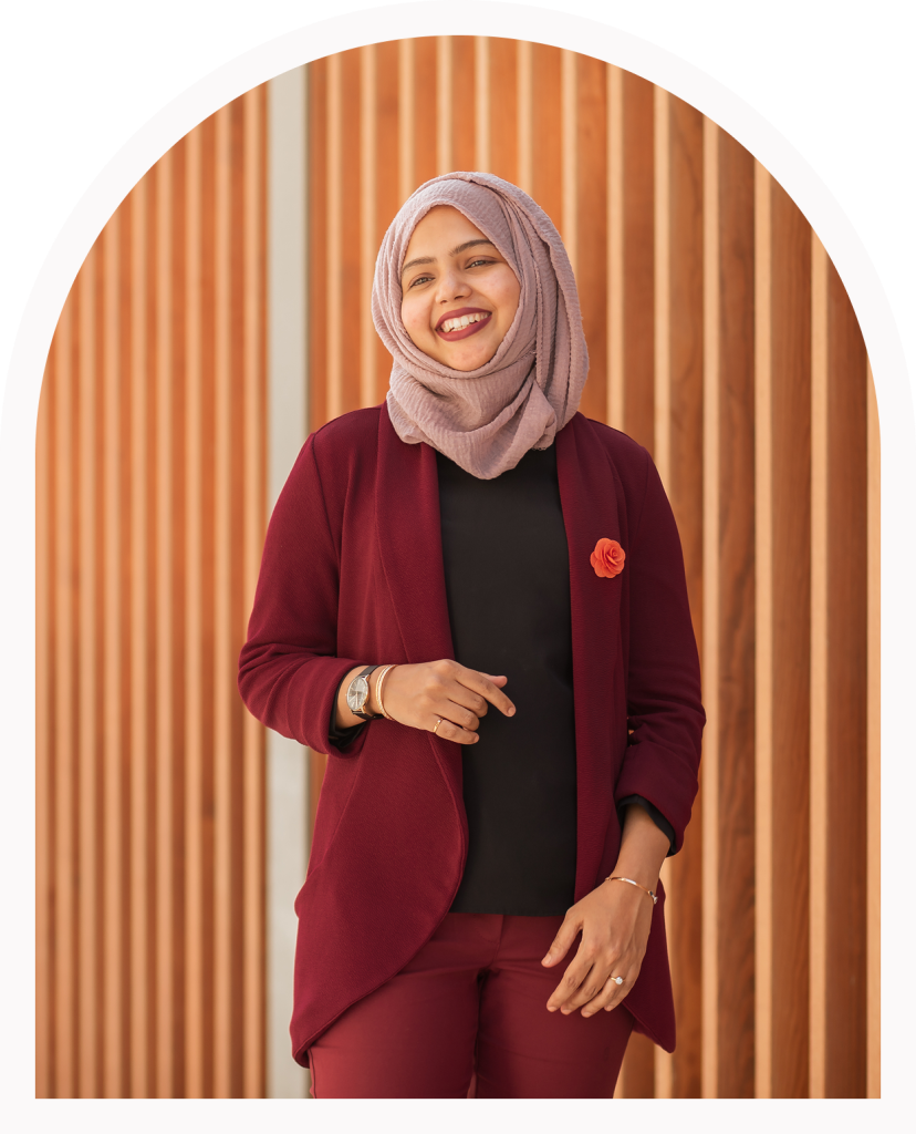 A female concierge in a taupe headscarf and red blazer smiles at the camera
