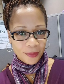 Close-up of a person wearing a purple top and a shiny purple scarf with layered necklaces, sitting in an office cubicle.