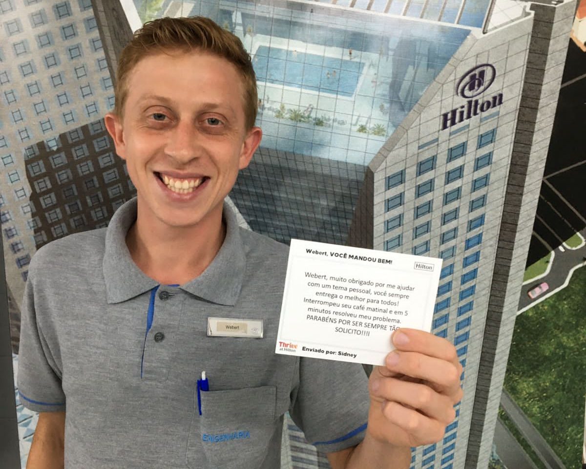Webert stands in front of a Hilton Sao Paulo Morumbi display, holding a recognition card.